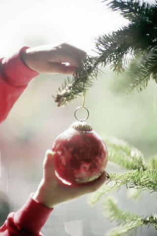 Foto: Ein Kind hängt eine rote Weihnachtskugel an einen Tannenbaum.