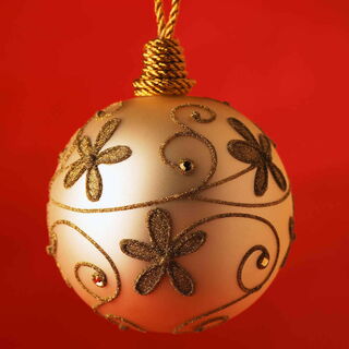 Foto: Eine beigefarbene reich verzierte Weihnachtskugel vor rotem Hintergrund.