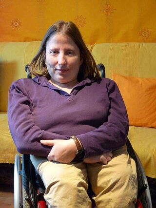 Foto: Ein Portrait von Evelyn in ihrem Rolli in meinem Snoozleraum. Sie hat ihre Arme vor dem Körper verschränkt.