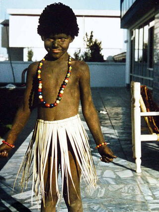 Foto: Ich bin komplett braun bemalt, trage nur ein Baströckchen und eine bunte Perlenkette um den Hals.