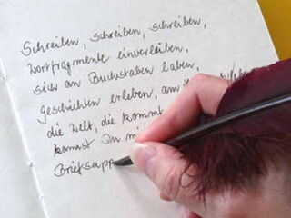 Foto: Eine andere Schreibmaus schreibt mit Tinte und Feder einen Text in ein Buch.