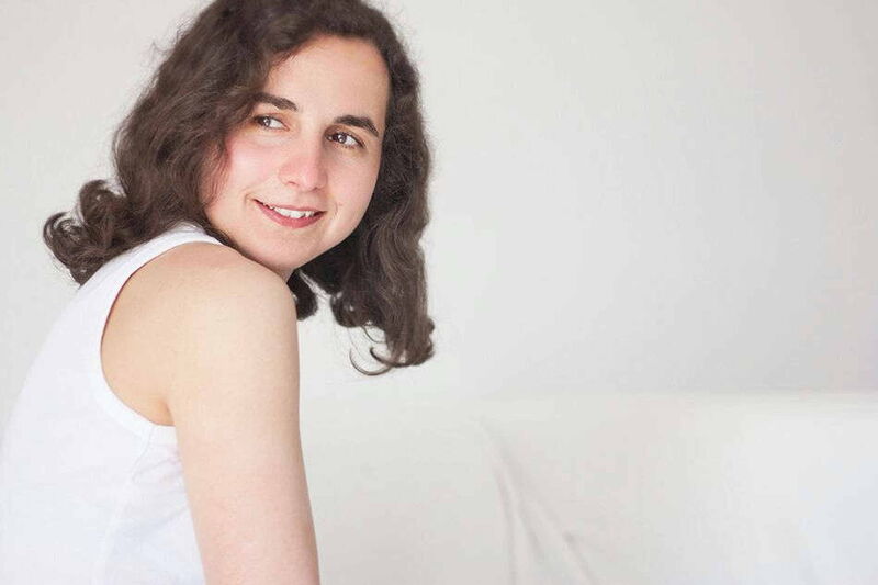 Foto: Mio im weißen Trägershirt hat den Kopf nach rechts gedreht und schaut rechts an der Kamera vorbei.