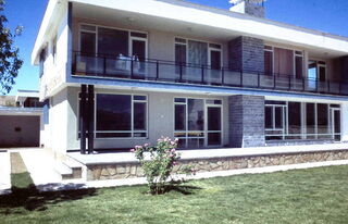 Foto: Ein zweistöckiger Bungalow mit Flachdach und im Vordergrund ein großer Rasen.