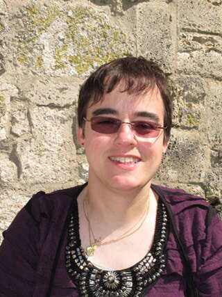 Foto: Die Uschimaus in einem schönen, reich verzierten Trachten-Oberteil vor einer Mauer.