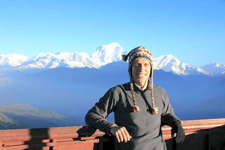 Foto: Benjamin mit Zipfelmütze vor einer schneebedeckten Bergkette im Himalaya.