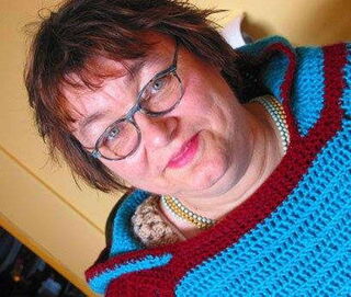 Foto: Anneli mit rötlichen Haaren und Brille in einem ihrer selbstgehäkelten Ponchos.