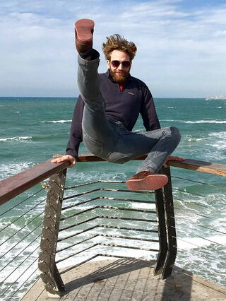 Foto: Benjamin stützt sich mit den Armen am Geländer ab und schmeißt die Beine in die Luft. Im Hintergrund das Meer.