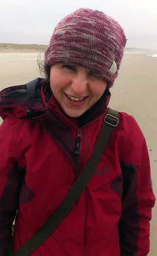 Foto: Die Mio-Maus wind- und wetterfest mit rot-violettem Anorak und lila Strickmütze an der Nordseeküste.