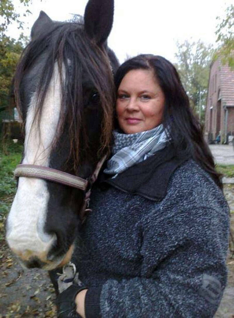 Foto: Suta Wanji aus der Halbdistanz mit dunkelblauer Flanelljacke und ihrem Pferd Buffy an der rechten Seite.