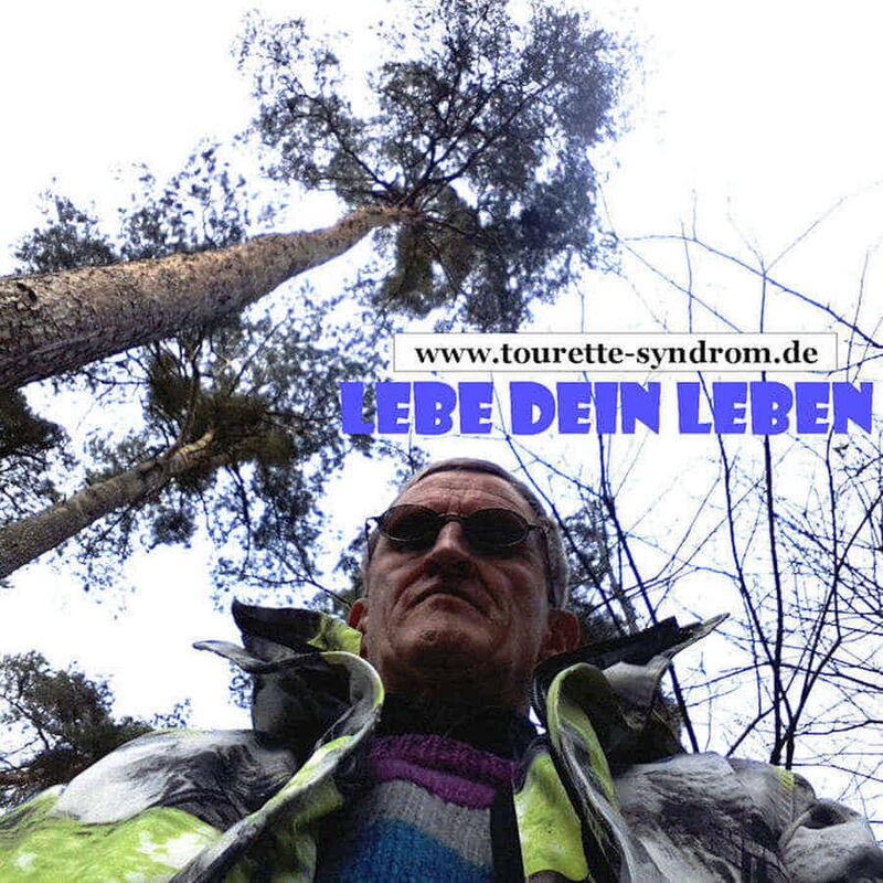 Foto: Hermann unter hohen Bäumen. Das Foto zeigt Hermann's Oberkörper und die Baumspitzen von unten nach oben.