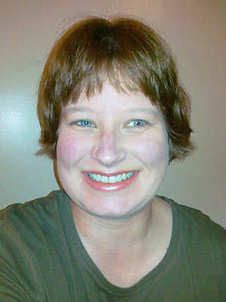 Foto: Susanne in einem jägergrünen T-Shirt legt ihr breitestes Grinsen auf.